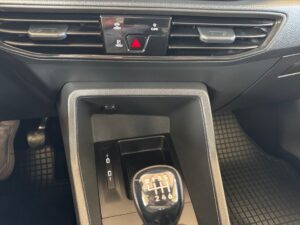 Manueller Schalthebel in einem Auto, umgeben von schwarzen Armaturenbrettdetails.
